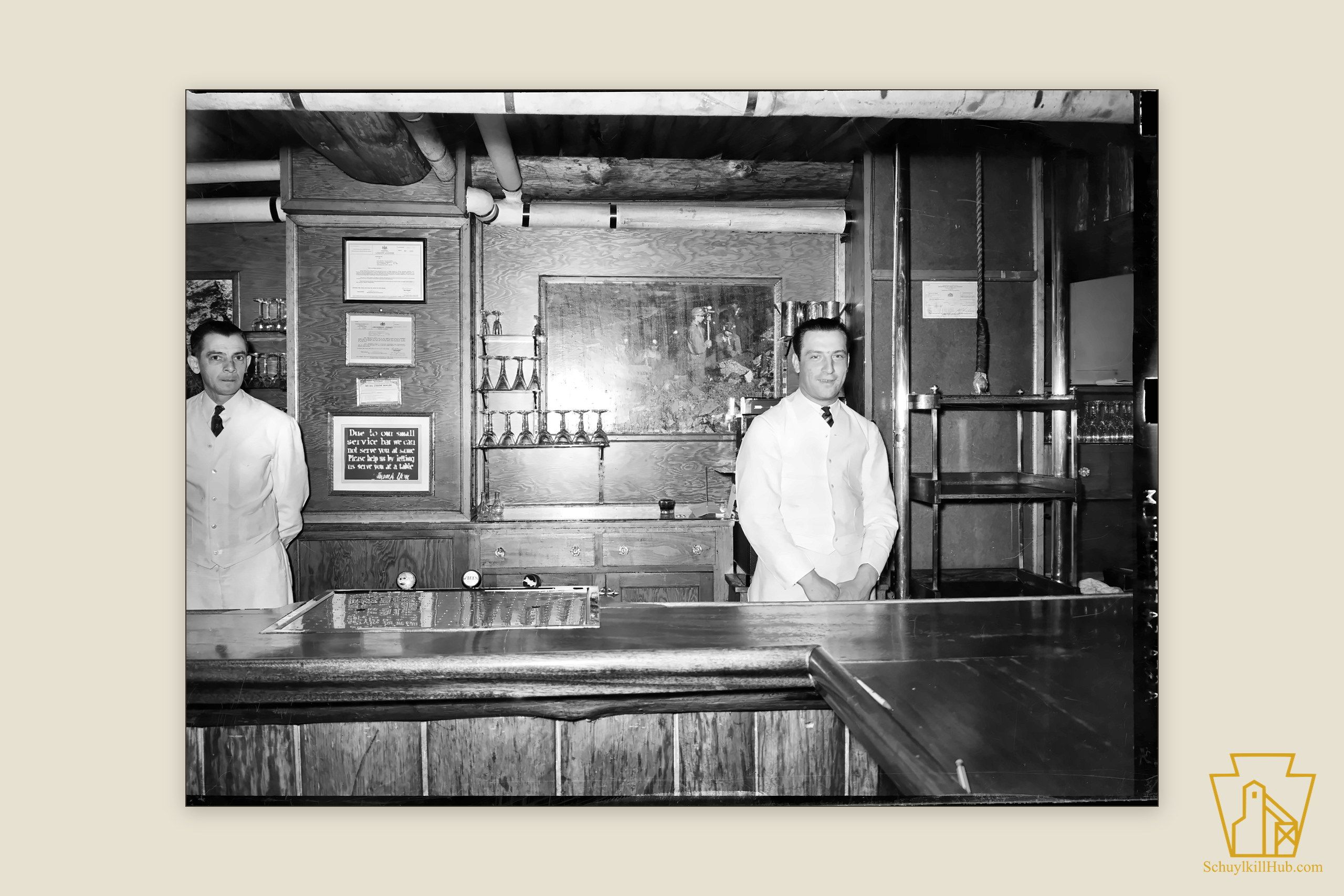 Two bartenders in white jackets behind the long polished bar of the Necho Allen Hotel.