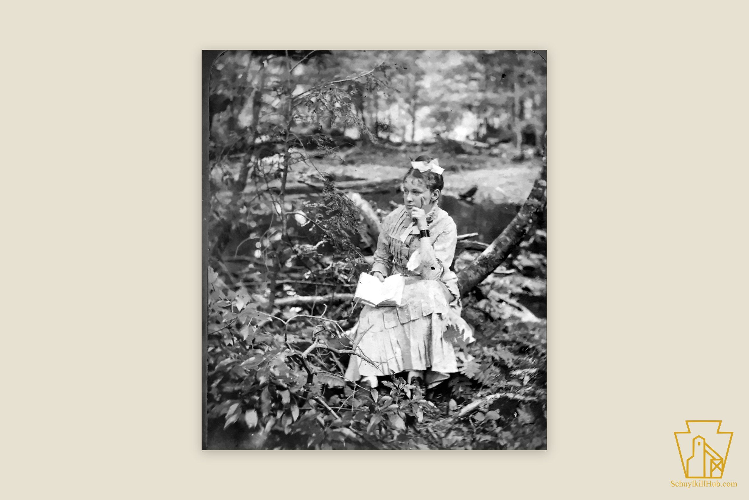 A young woman seated reading a book in a woodland — a stereograph frame by George M. Bretz.