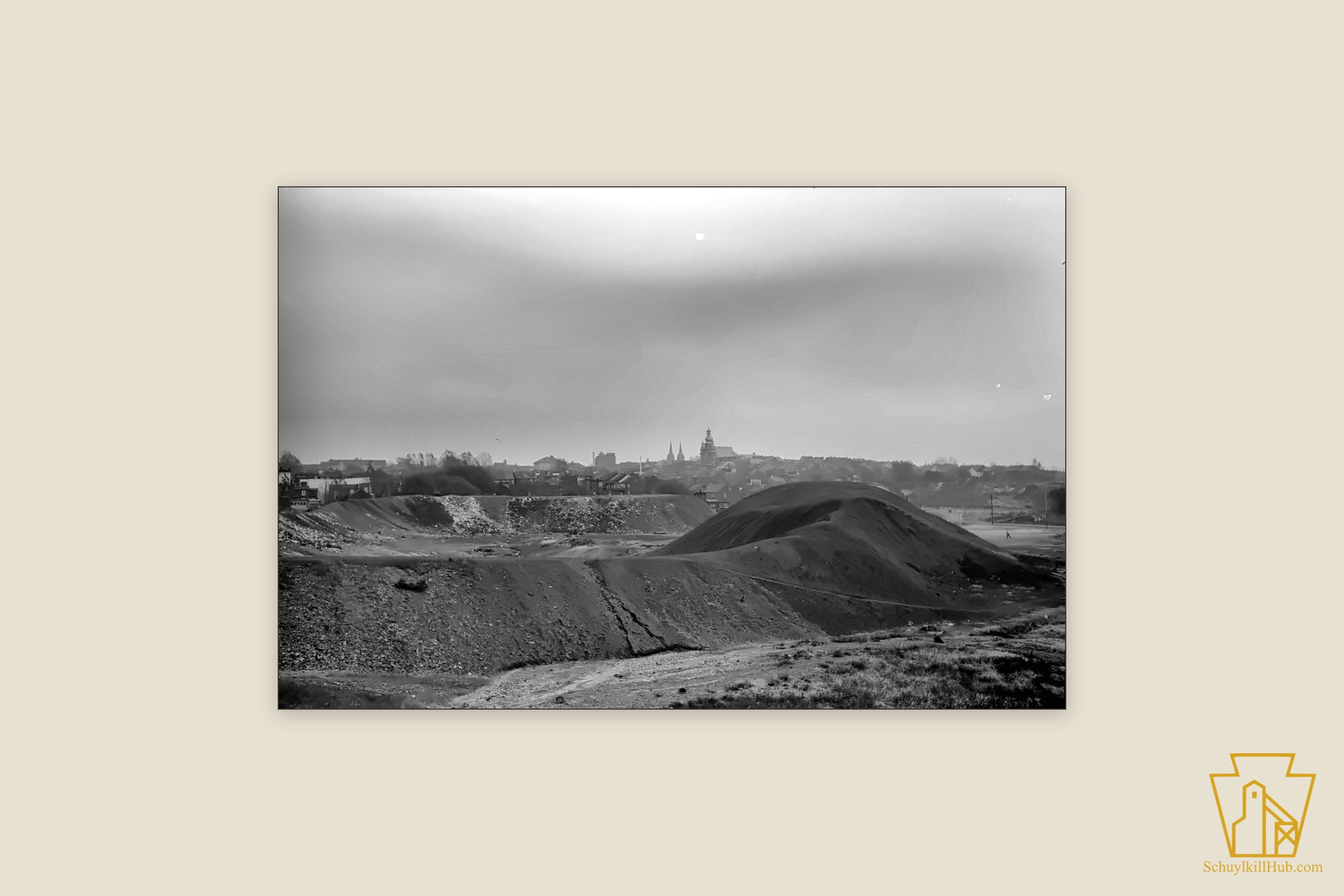Rooftops and church spires of a mining town crowded by culm banks and stripped ground.
