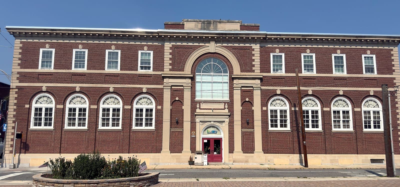 The Pottsville Free Public Library at 215 West Market Street, seen head-on from the brick plaza across Third Street: a symmetrical two-story red-brick Georgian Revival library with light stone trim, a tall central Palladian window above the main entrance, and round-arched windows across both ground-floor wings.