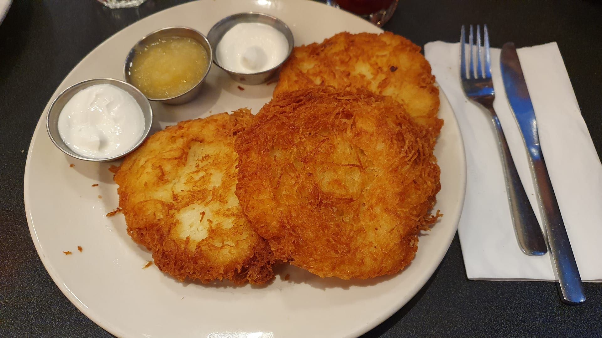 Three crisp, deep-golden bleenies on a diner plate with cups of sour cream and applesauce.