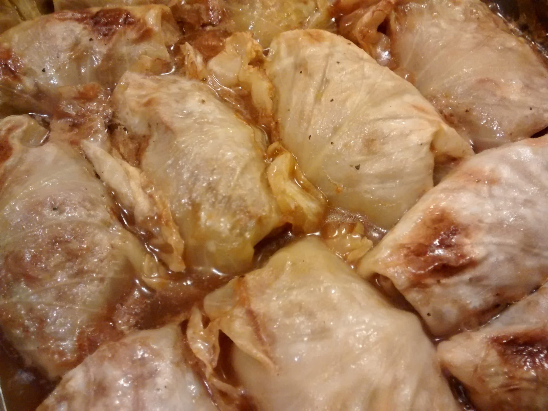 Halupki packed side by side in a baking dish, the cabbage rolls braised soft in tomato sauce.