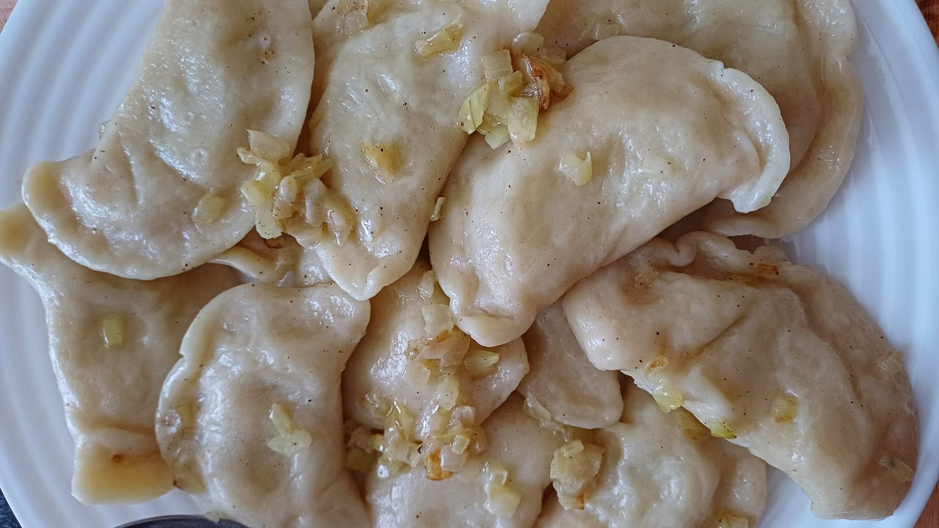 Boiled pierogies piled on a white plate, glossy with butter and topped with sautéed onions.