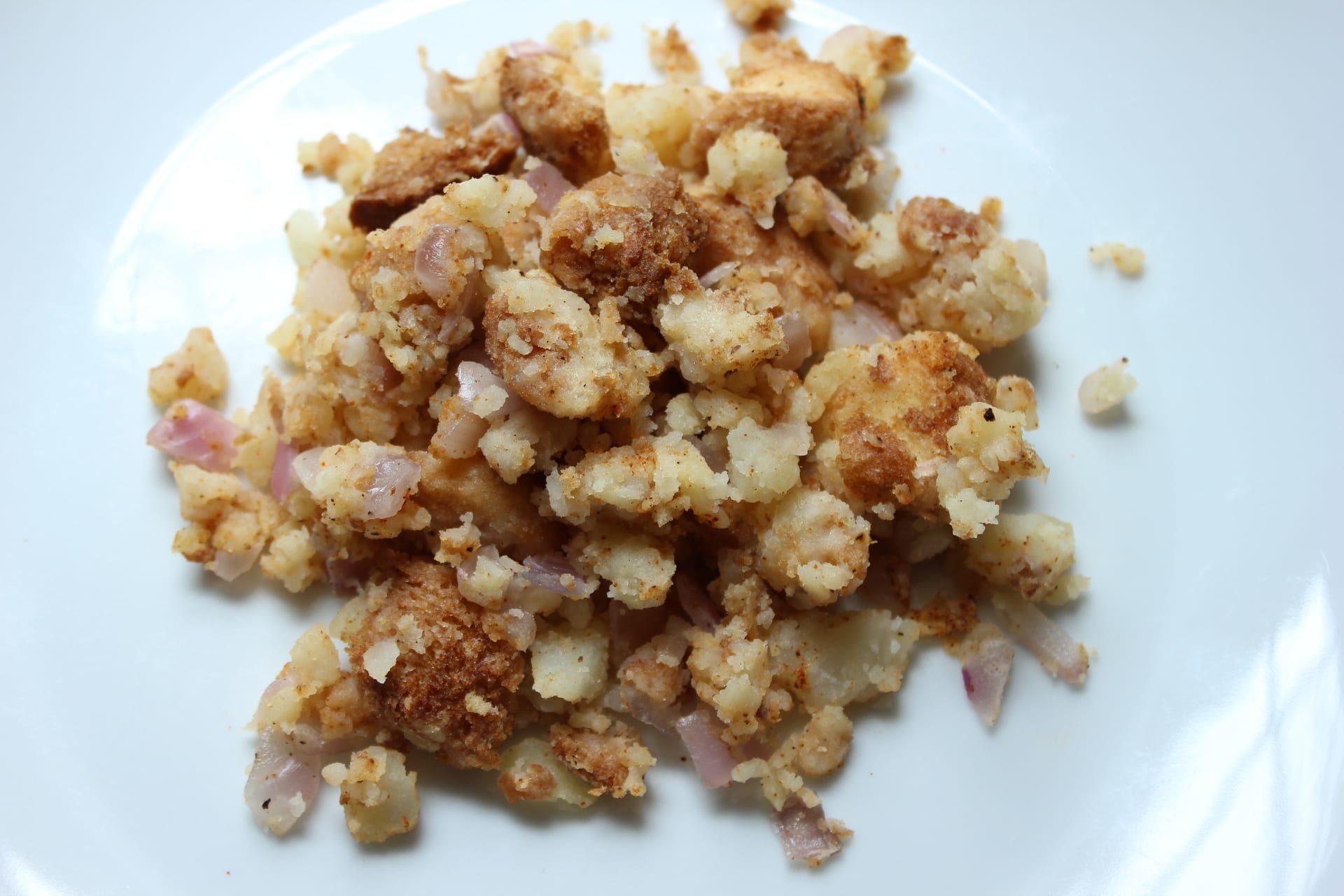 A scoop of potato filling on a white plate — mashed potato and bread cubes browned with onion.