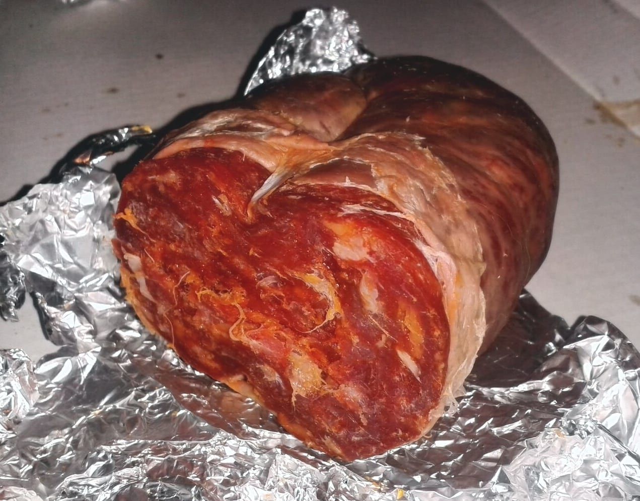 A whole dry-cured soupie on its foil wrapper, the cut end showing a deep-red interior.