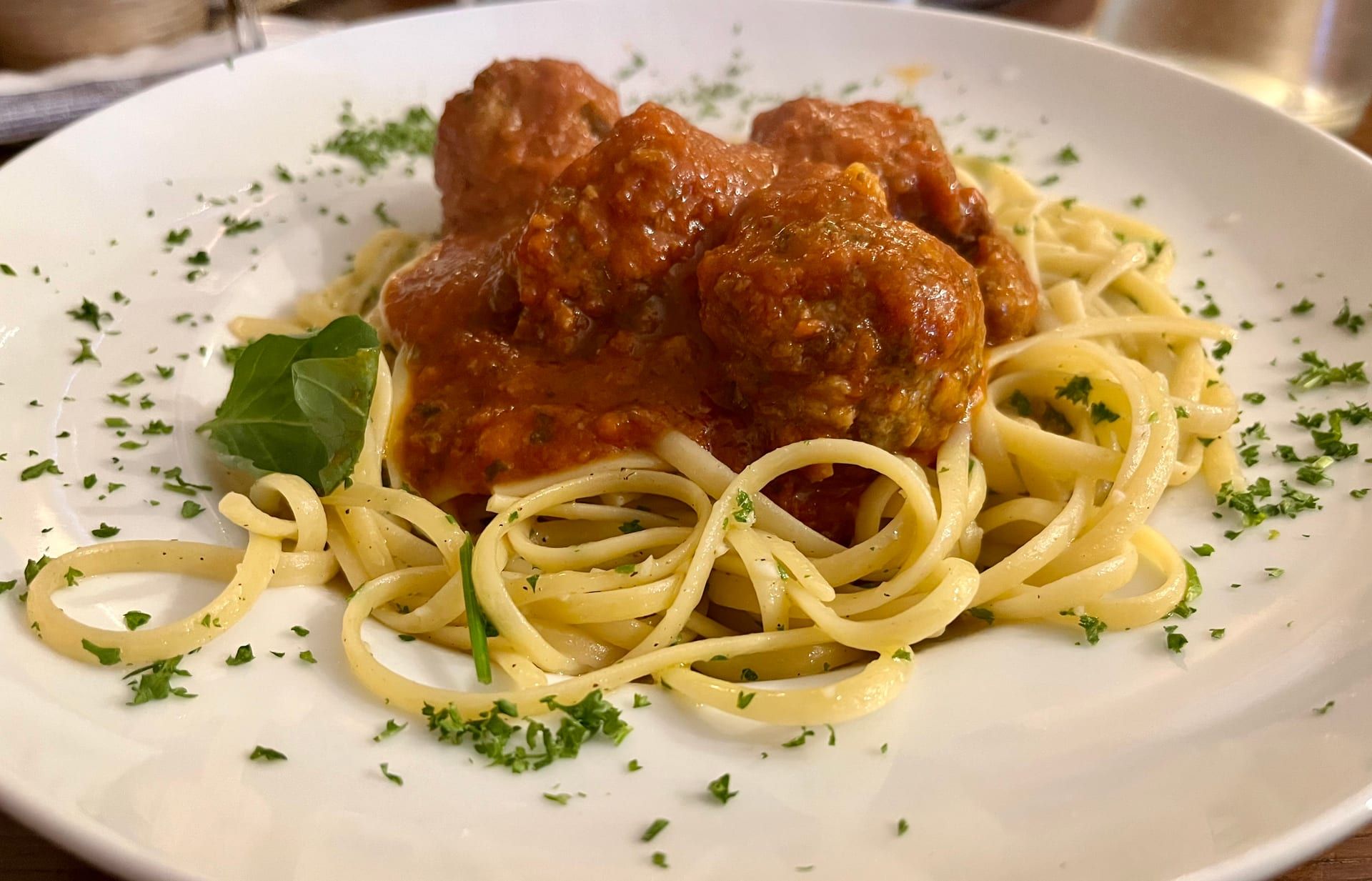 Meatballs in red sauce over long pasta, sprinkled with chopped parsley.