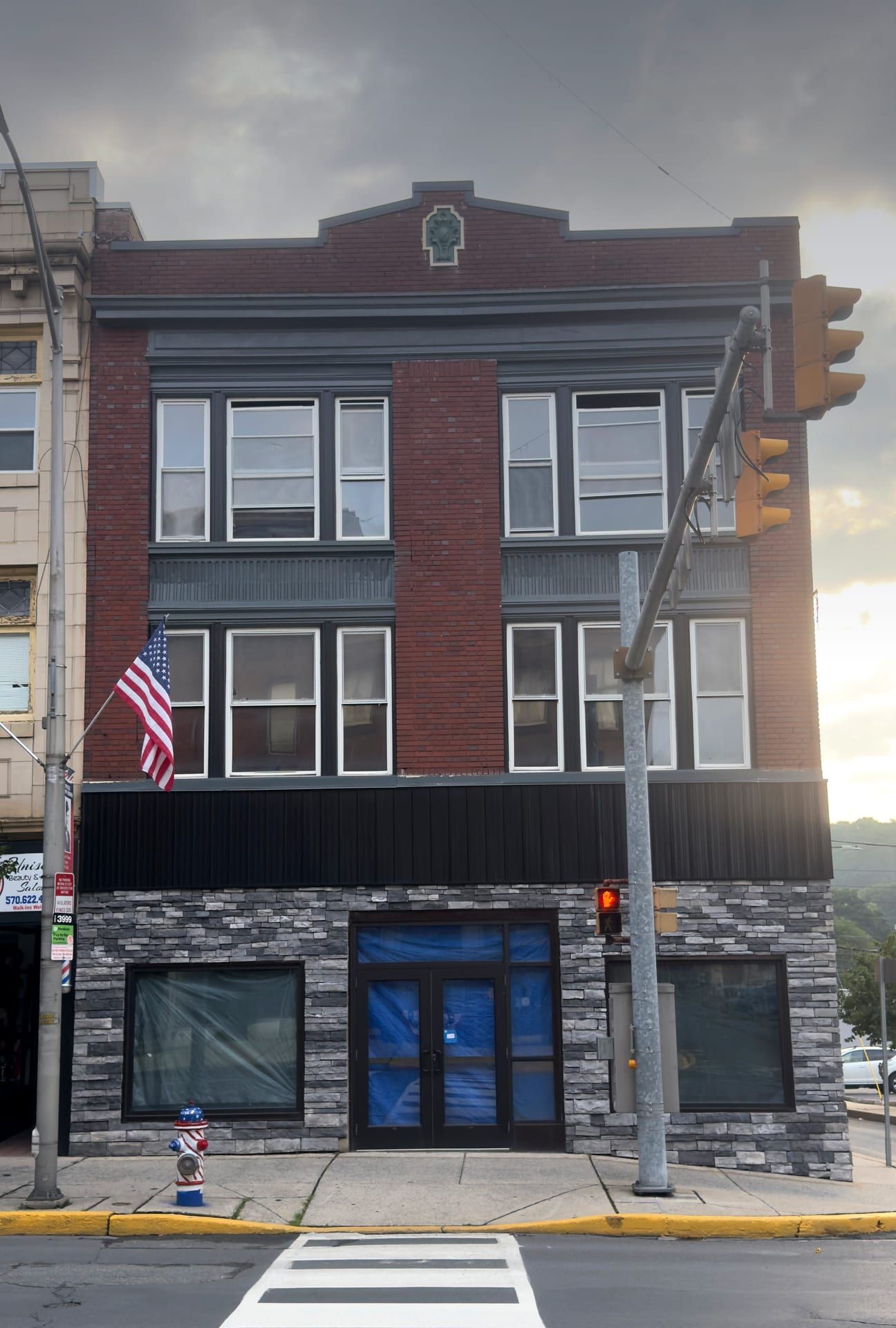 The vacant three-story brick corner block at 200 North Centre Street, its ground-floor storefronts papered over below a stepped brick parapet centered on a green ornament.