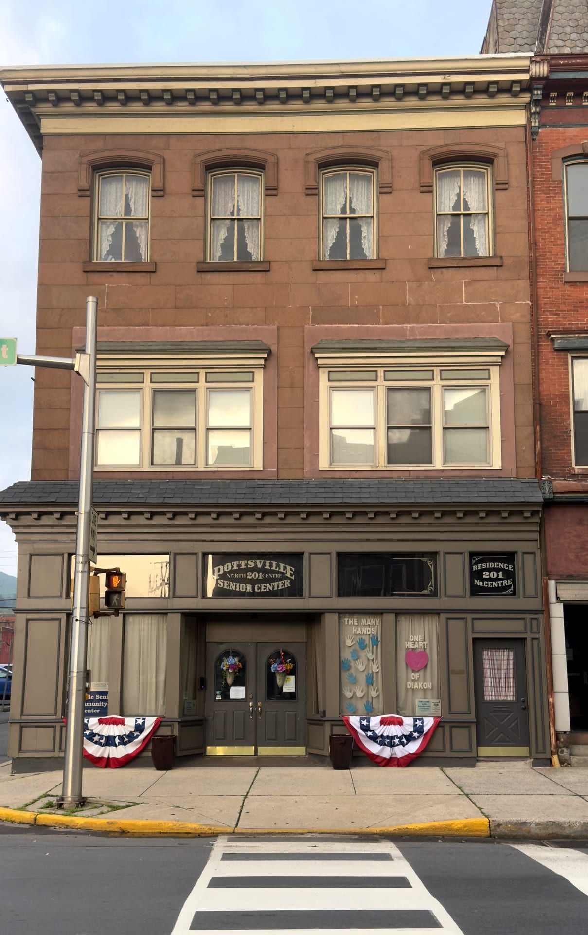 The three-story bracketed-cornice building at 201 North Centre Street, its ground-floor windows lettered for the Pottsville Senior Community Center and dressed with patriotic bunting.