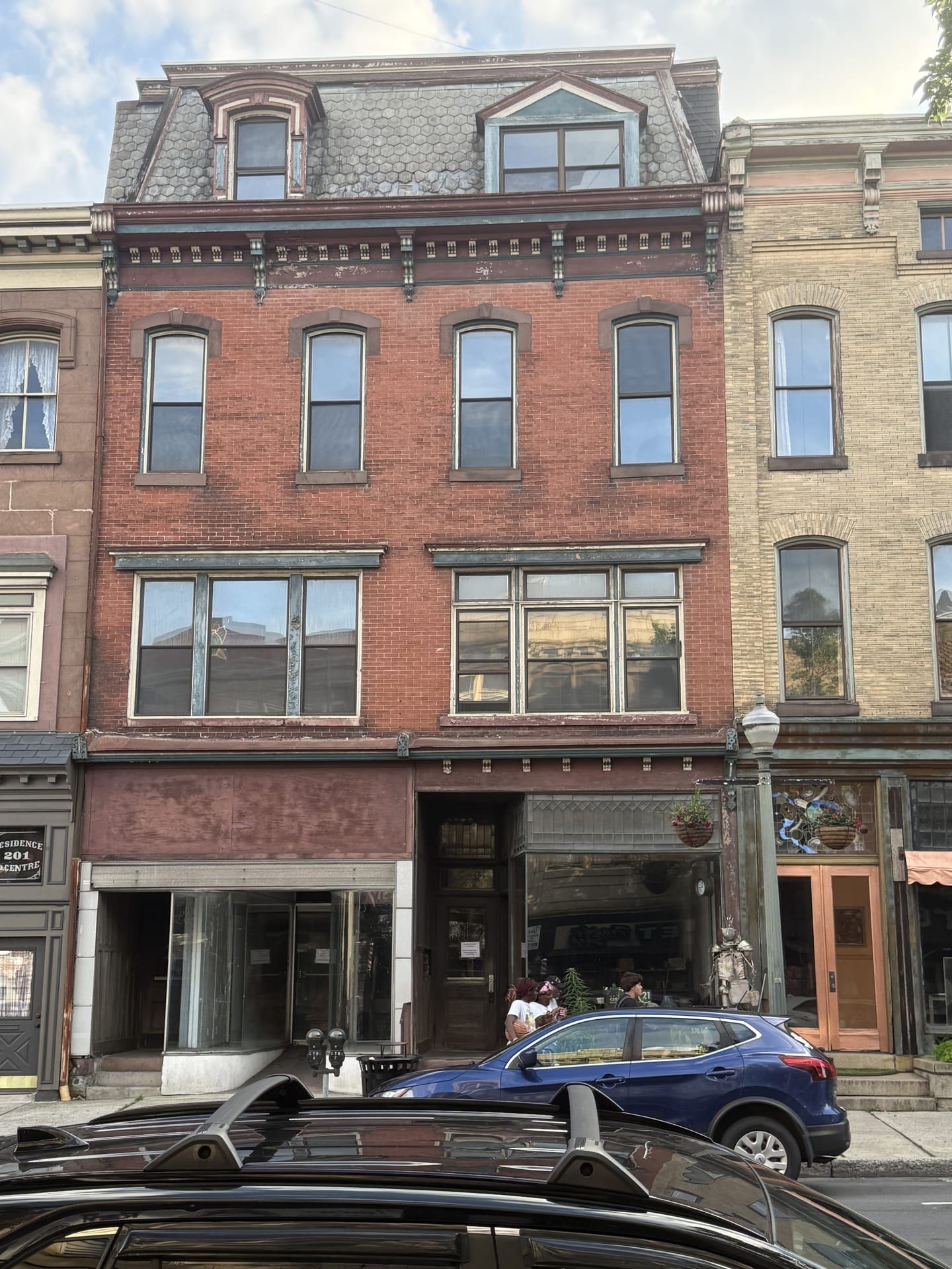 203 North Centre Street, Pottsville — a three-story red-brick Second Empire commercial building with a slate mansard roof, one dormer, and a bracketed cornice, standing between the corner building at 201 and the buff-brick Ulmer Building; a Century 21 for-sale sign stands in the vacant storefront window.
