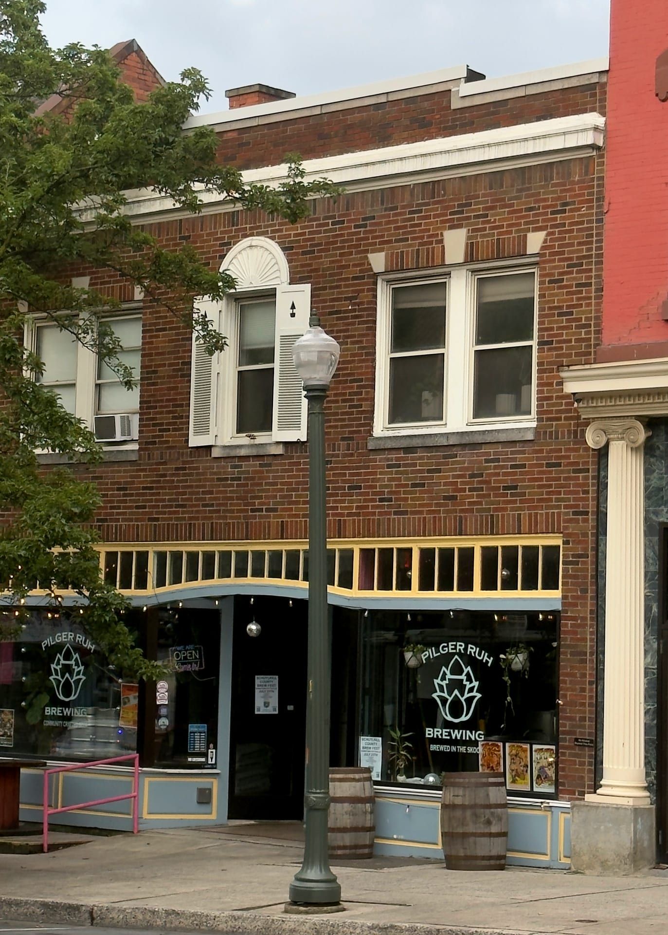 The two-story brick building at 213–215 North Centre Street, its storefront windows bearing the Pilger Ruh Brewing hop-leaf logo below a second-floor window with a semicircular fanlight.