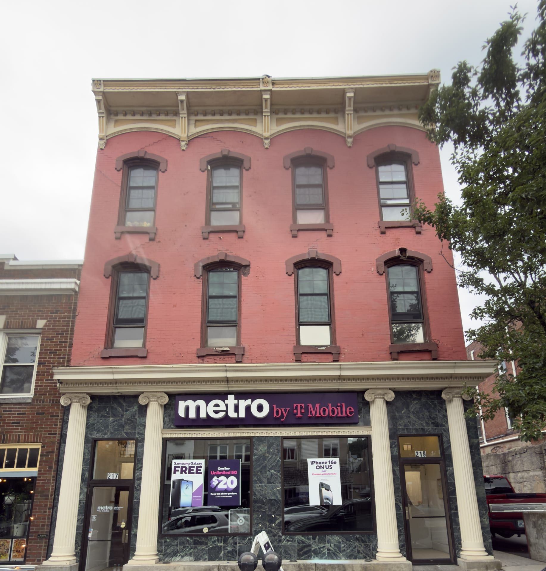 The three-story red-brick front of 217–219 North Centre Street, Pottsville: two floors of hooded windows beneath a heavy bracketed wooden cornice, over a ground-floor storefront framed by cream-colored Ionic columns and a dark green marble base; a purple 'metro by T-Mobile' sign spans the storefront, with the entrance to 217 at left and 219 at right.