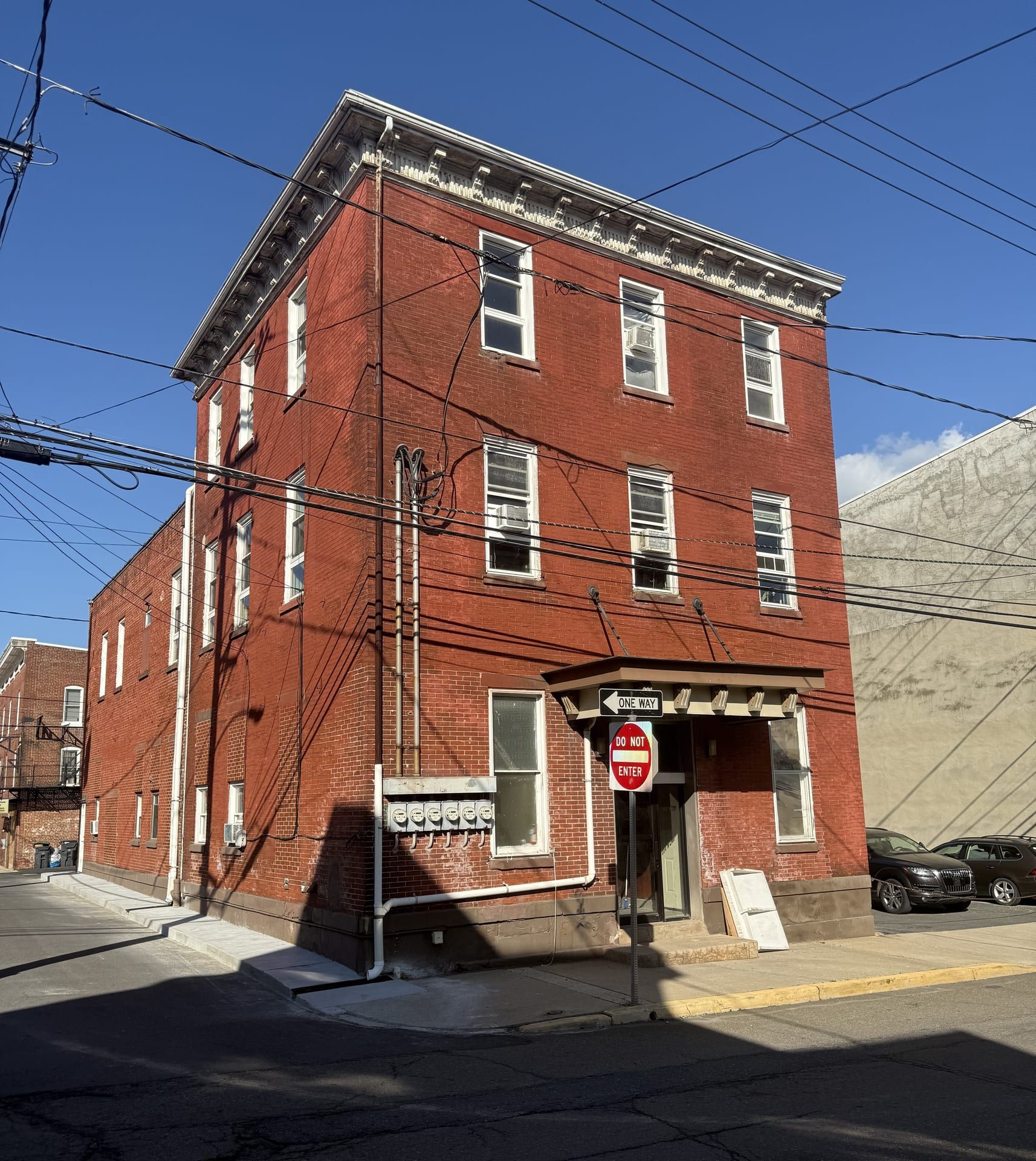 The corner of Second and Race streets: a three-story red brick house with a bracketed cornice and a hooded corner doorway, a row of electric meters on its side wall, and a lower two-story rear section behind.