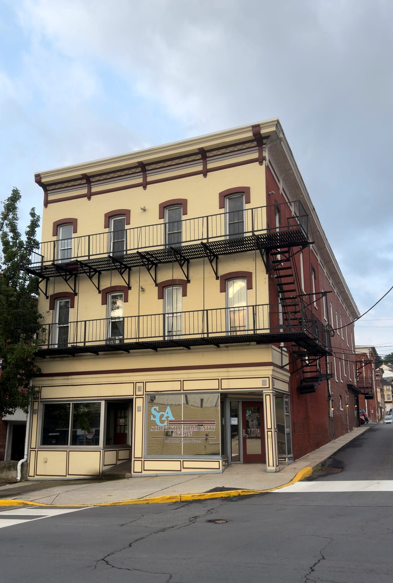 The three-and-a-half-story Italianate corner building at 225 North Centre Street, cream-painted with red trim, a bracketed cornice and two tiers of iron balconies, its ground floor lettered 'Schuylkill Community Action.'