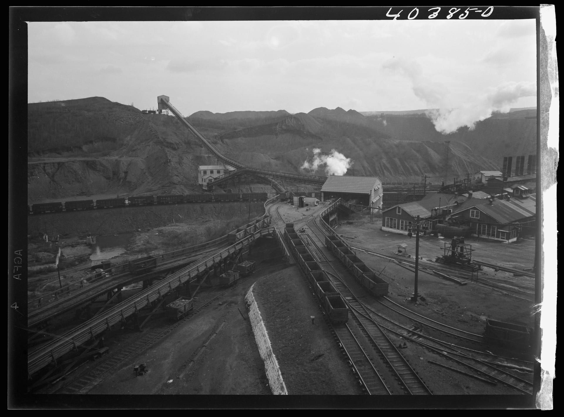 A 1938 elevated view of the Saint Nicholas breaker complex at Gilberton: a long inclined conveyor and culm banks above a yard of loaded coal cars and colliery buildings, with steam rising in the distance.