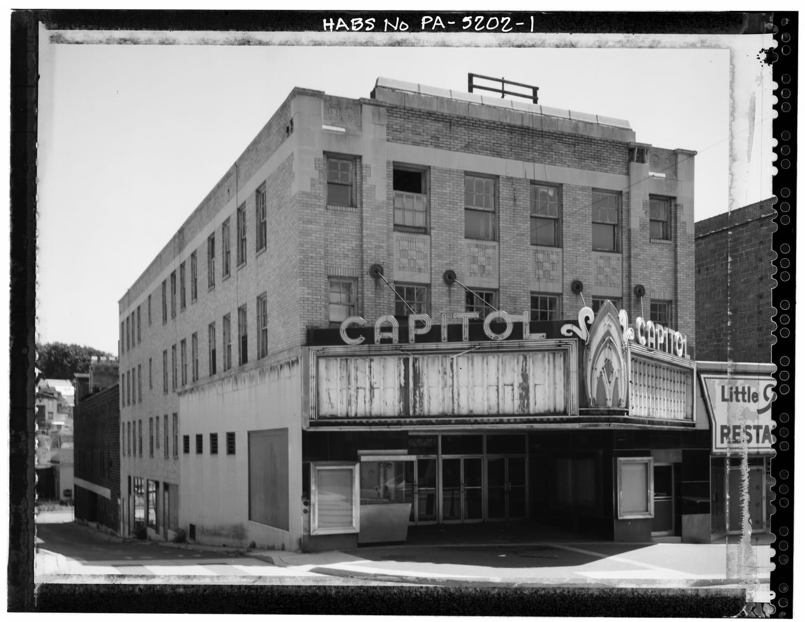 A three-quarter street view of the Capitol Theatre, its 'CAPITOL' marquee projecting over the sidewalk beneath a four-story brick facade.