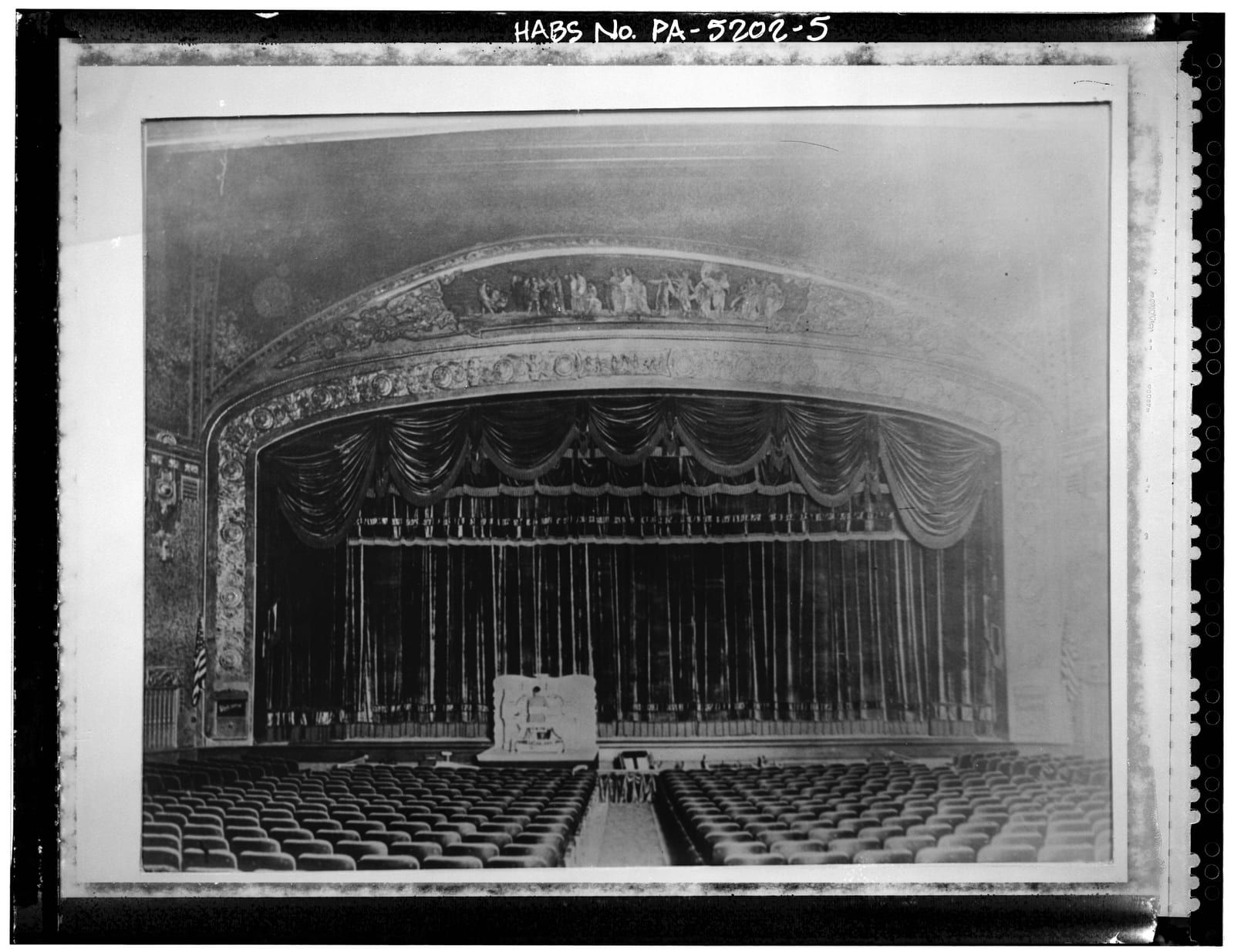 The Capitol Theatre auditorium: an ornamented proscenium arch framing a deeply draped stage curtain above rows of empty seats.