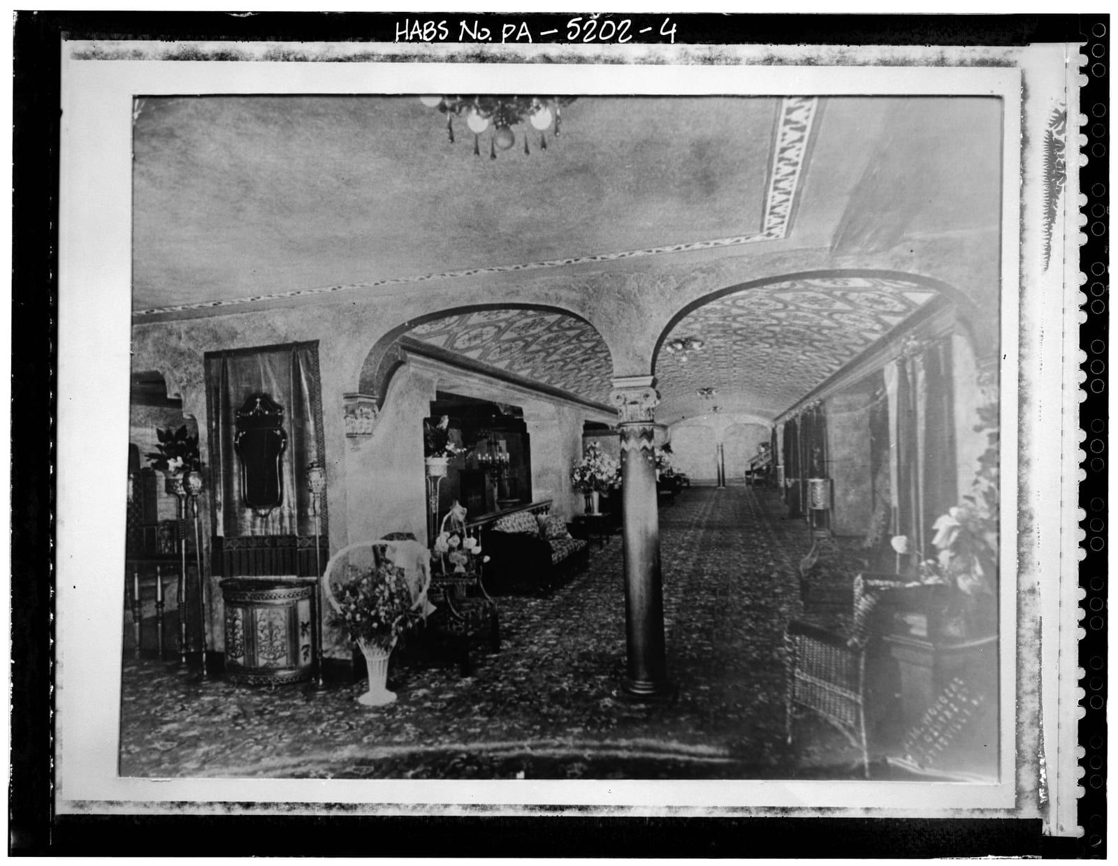 The Capitol Theatre's vaulted lobby, its arched latticework-ornamented plaster ceiling carried on a single ornate column, furnished with wicker seating and flowers.
