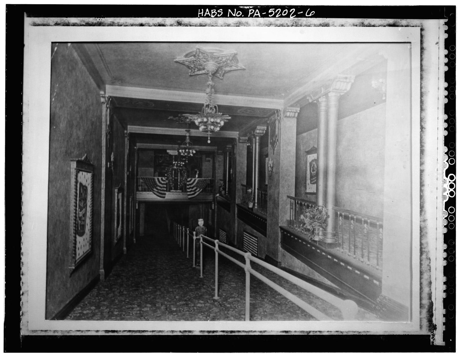 A mezzanine promenade inside the Capitol Theatre, lit by a chandelier beneath a star-shaped ceiling medallion, with columns and a balustrade overlooking the lobby below.