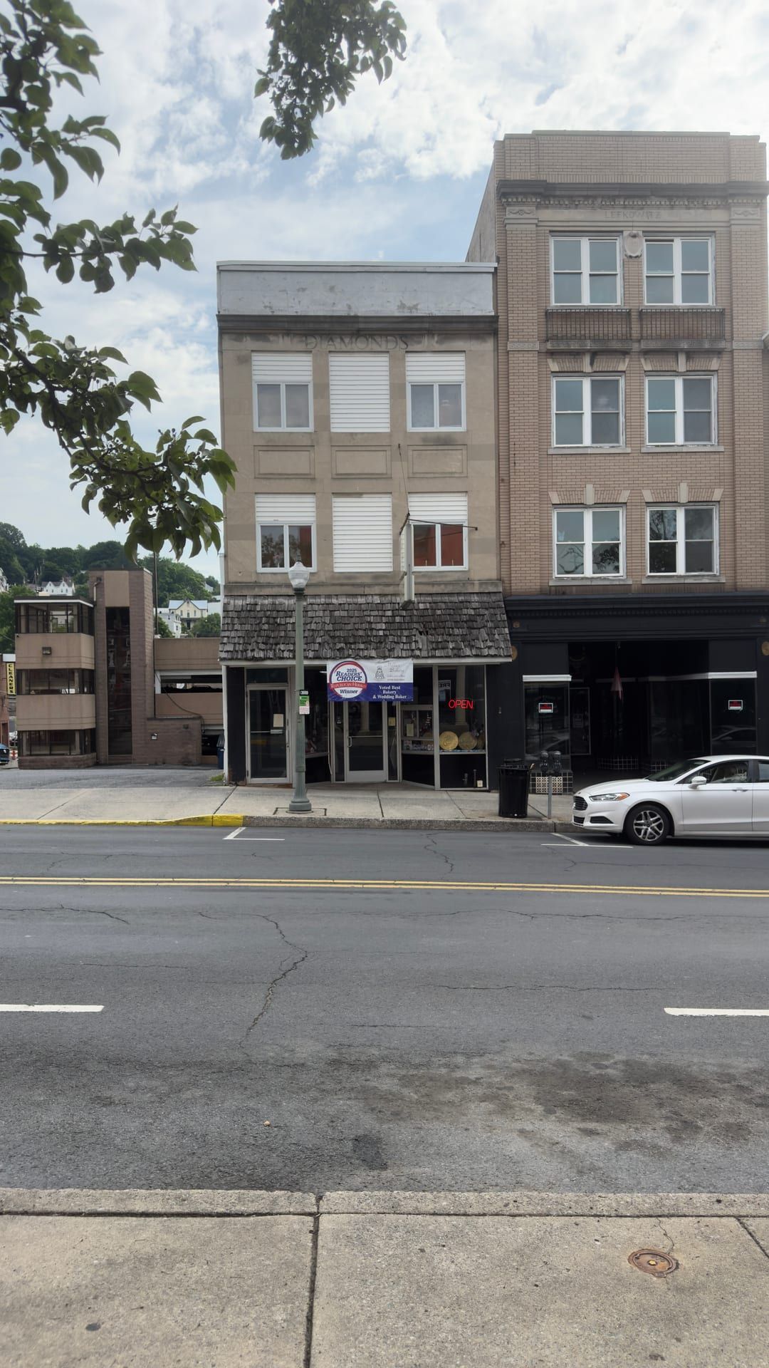 The three-story Diamonds Building at 216 North Centre Street, Pottsville — DIAMONDS carved in the stone frieze at the top of its facade, Momma Millie's Bakery in the storefront beneath a shingled pent awning — with the four-story Lefkowitz Building at right and the parking lot on the former Capitol Theatre site at left.