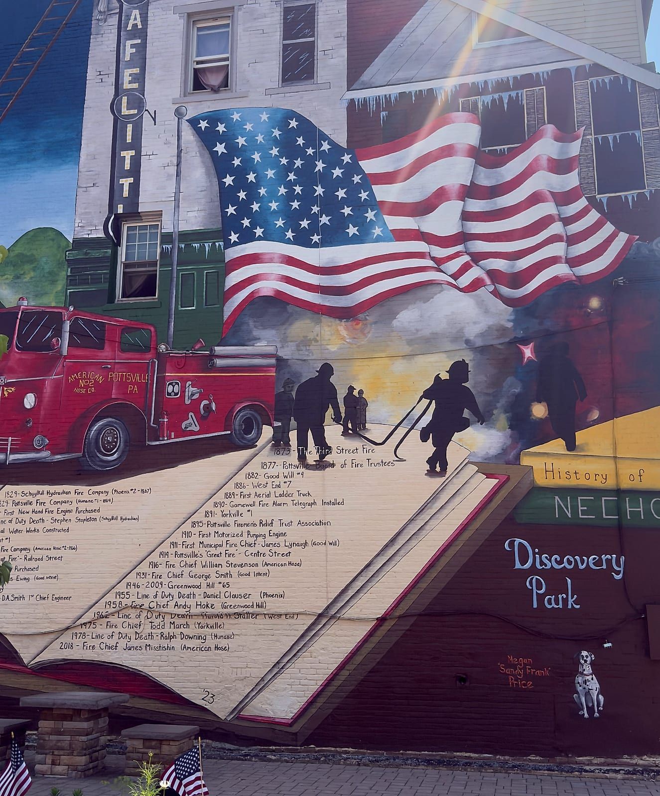 Megan Price's 2½-story firefighting-history mural at Discovery Park — a large American flag, a red 1948 American LaFrance engine of American Hose Co. No. 2, silhouetted firefighters, and a painted book timelining the city's fire companies from 1829 to 2018.