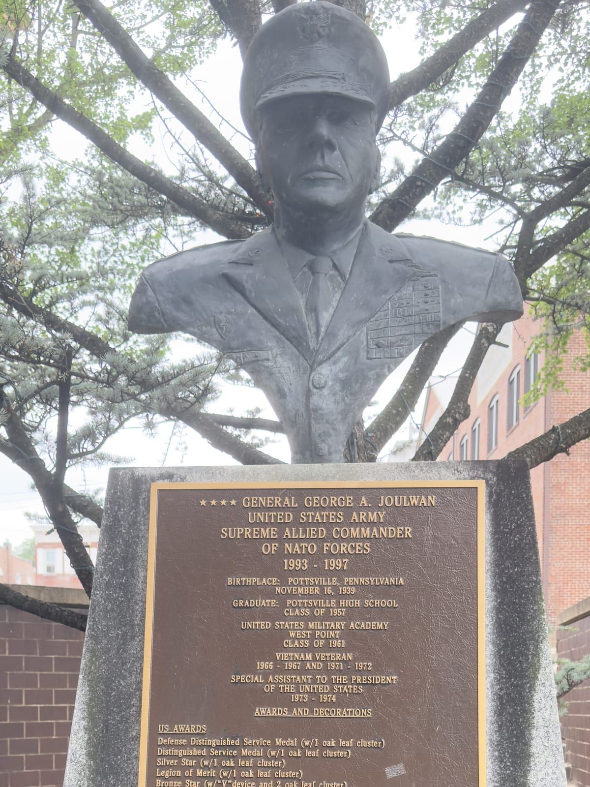 A bronze bust of General George A. Joulwan on a granite pedestal in Pottsville, in dress uniform and service cap, above a bronze plaque reading 'GENERAL GEORGE A. JOULWAN, UNITED STATES ARMY, SUPREME ALLIED COMMANDER OF NATO FORCES 1993-1997,' noting his Pottsville birth and his awards.