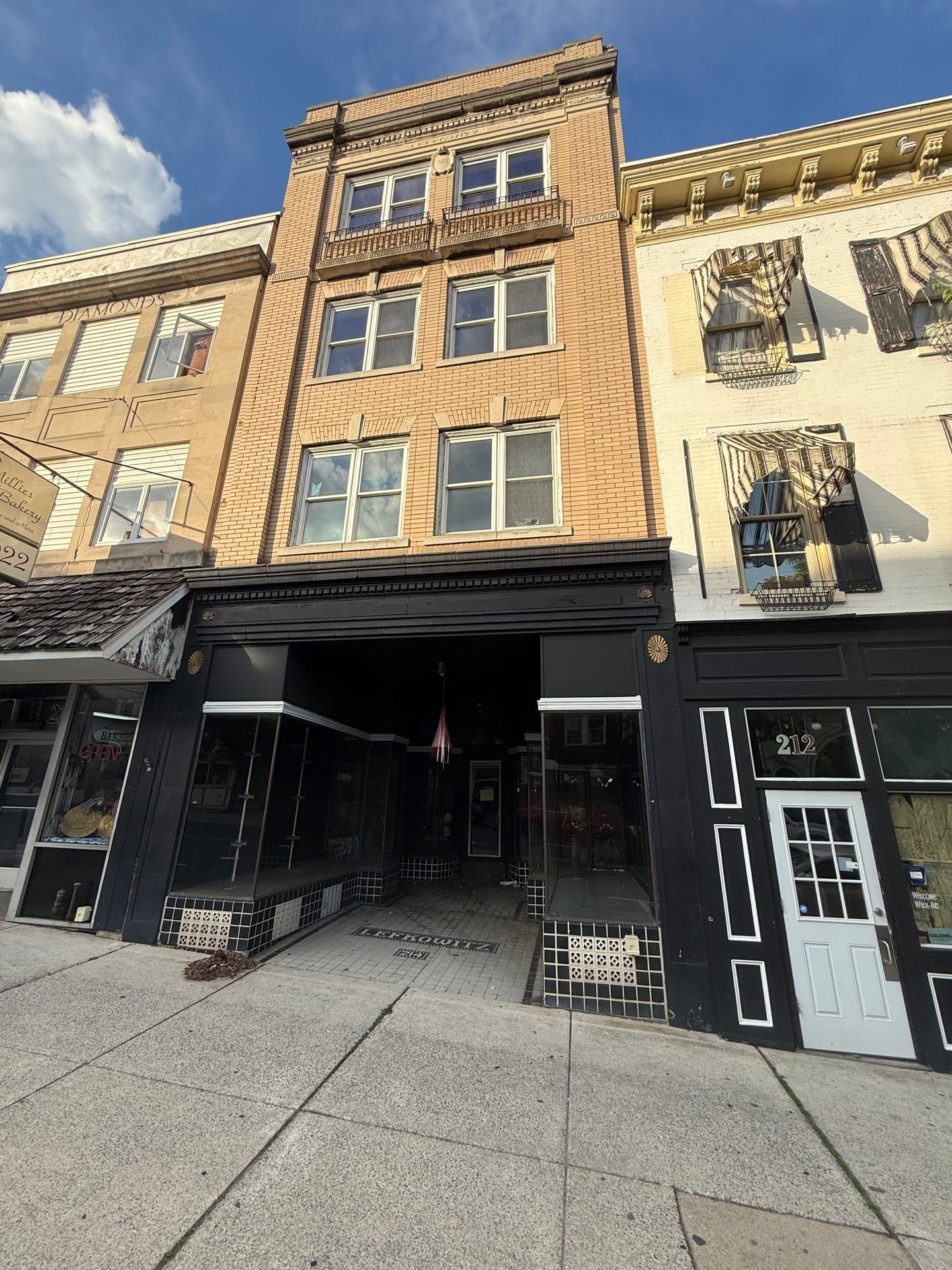 The Lefkowitz Building at 212–214 North Centre Street, Pottsville: a four-story buff-brick front with LEFKOWITZ and a 1925 date shield carved at the parapet, over a black-painted storefront with a deep recessed entrance; the three-story storefront of 212 at right.