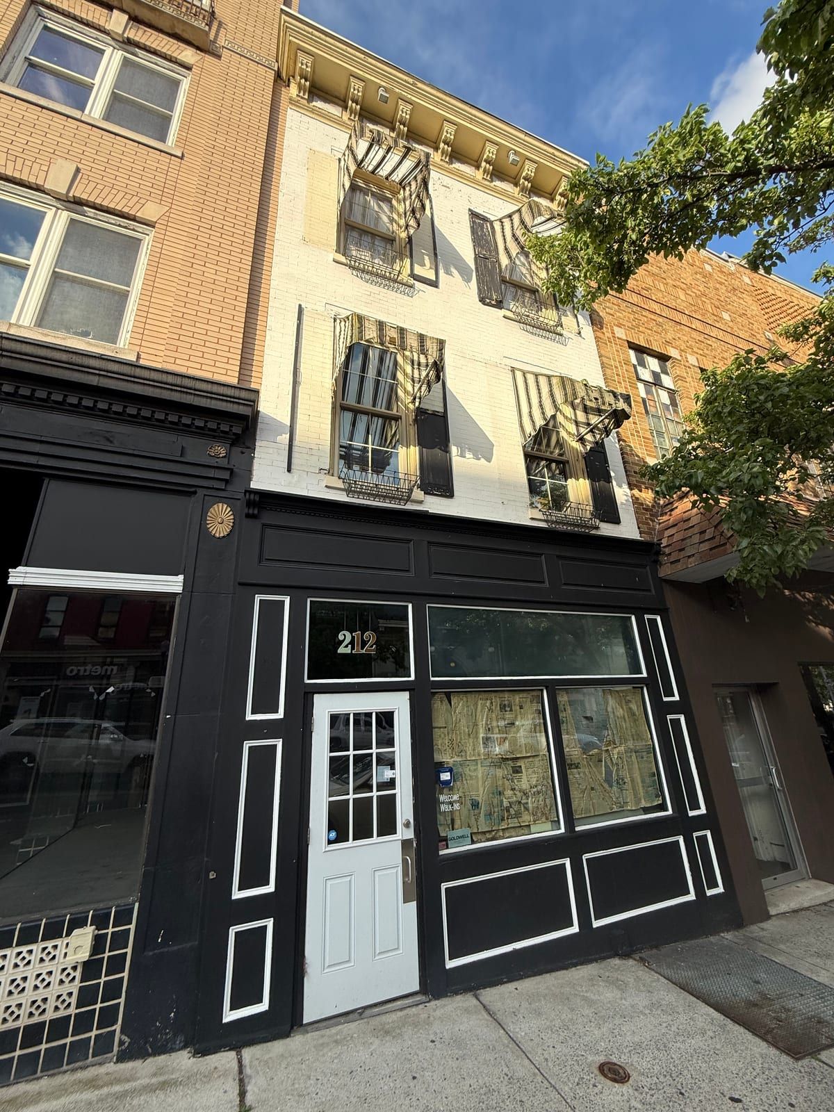 The storefront of 212 North Centre Street: a white six-pane door numbered 212 and a papered-over display window in a black-painted front, below two floors of white-painted brick with striped awnings.