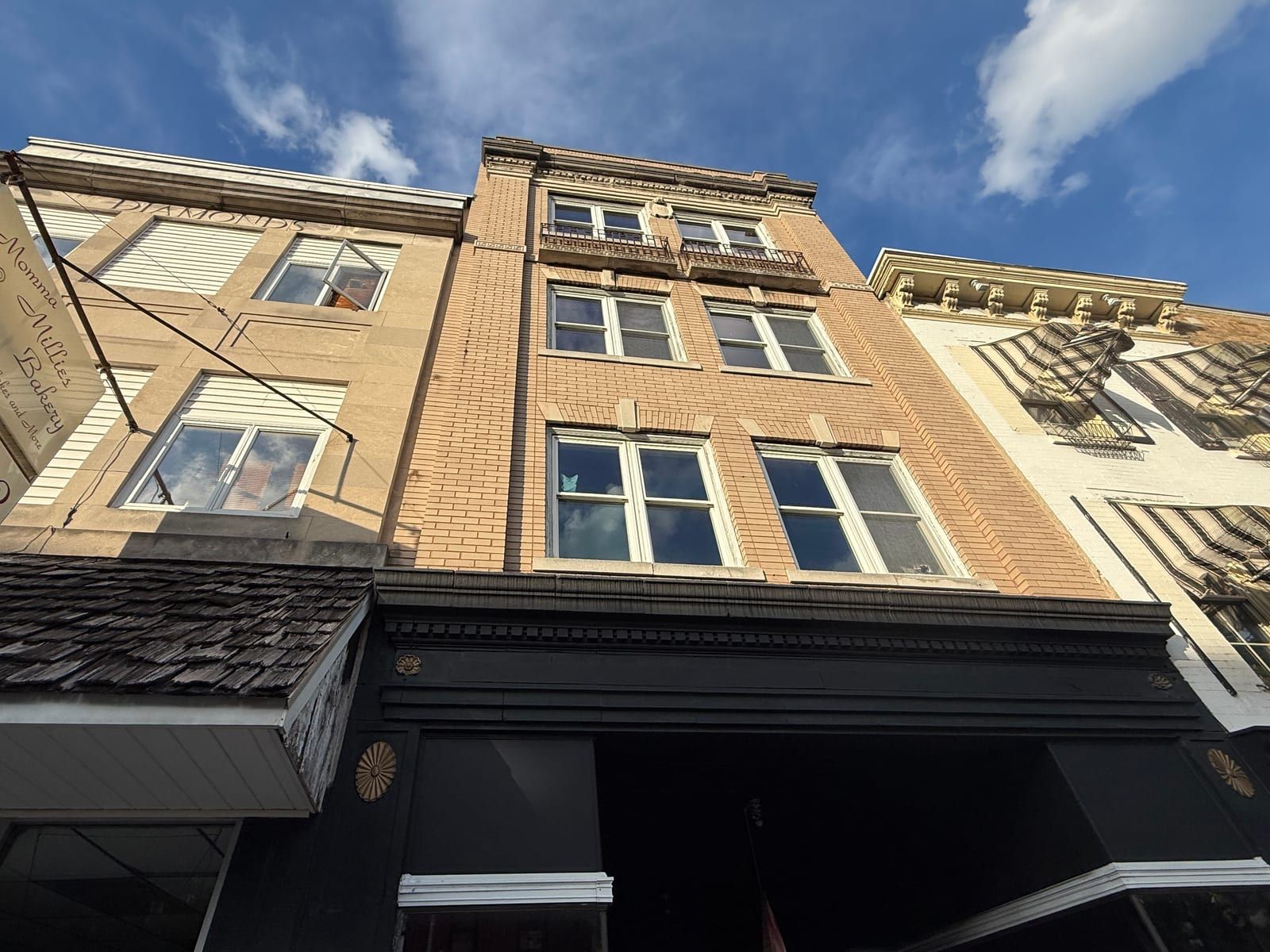The upper floors of the Lefkowitz Building from the sidewalk: buff brick with stone trim, a Greek-key band, iron window balconies, and a dentiled cornice above the black storefront fascia.