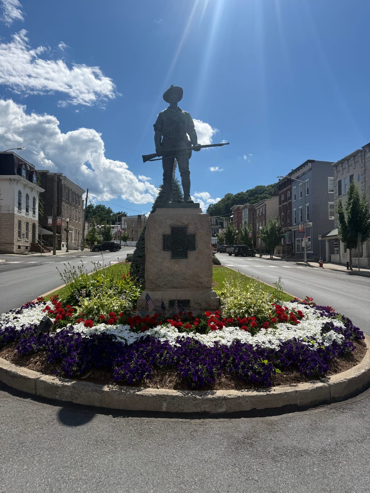 "The Hiker" — a bronze Spanish-American War infantryman in a campaign hat, his rifle held across his body, on a stone pedestal amid flowerbeds in Garfield Square, Pottsville.