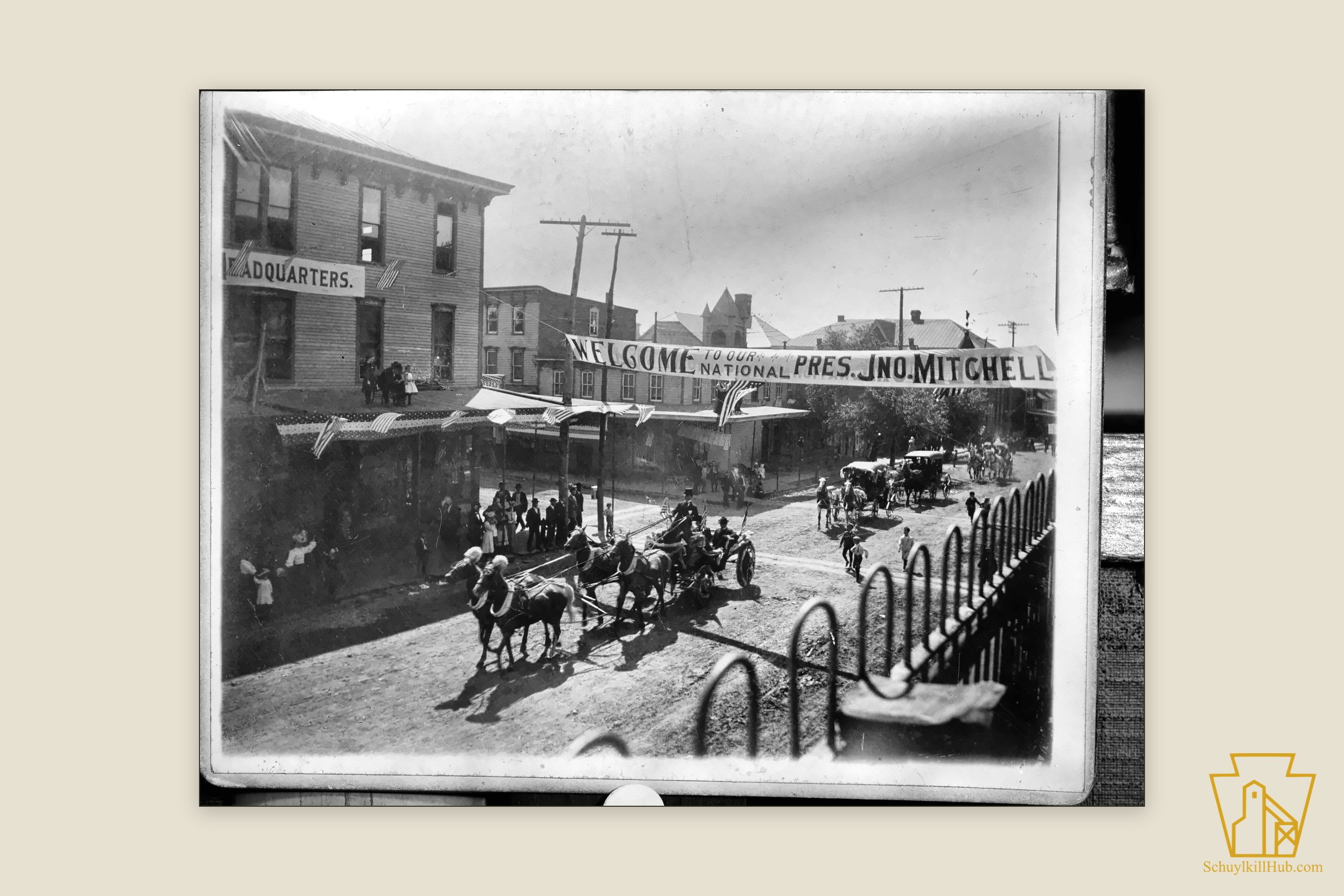 A banner spanning a Shenandoah street — ‘Welcome to our National Pres. Jno. Mitchell’ — over a horse-drawn procession.