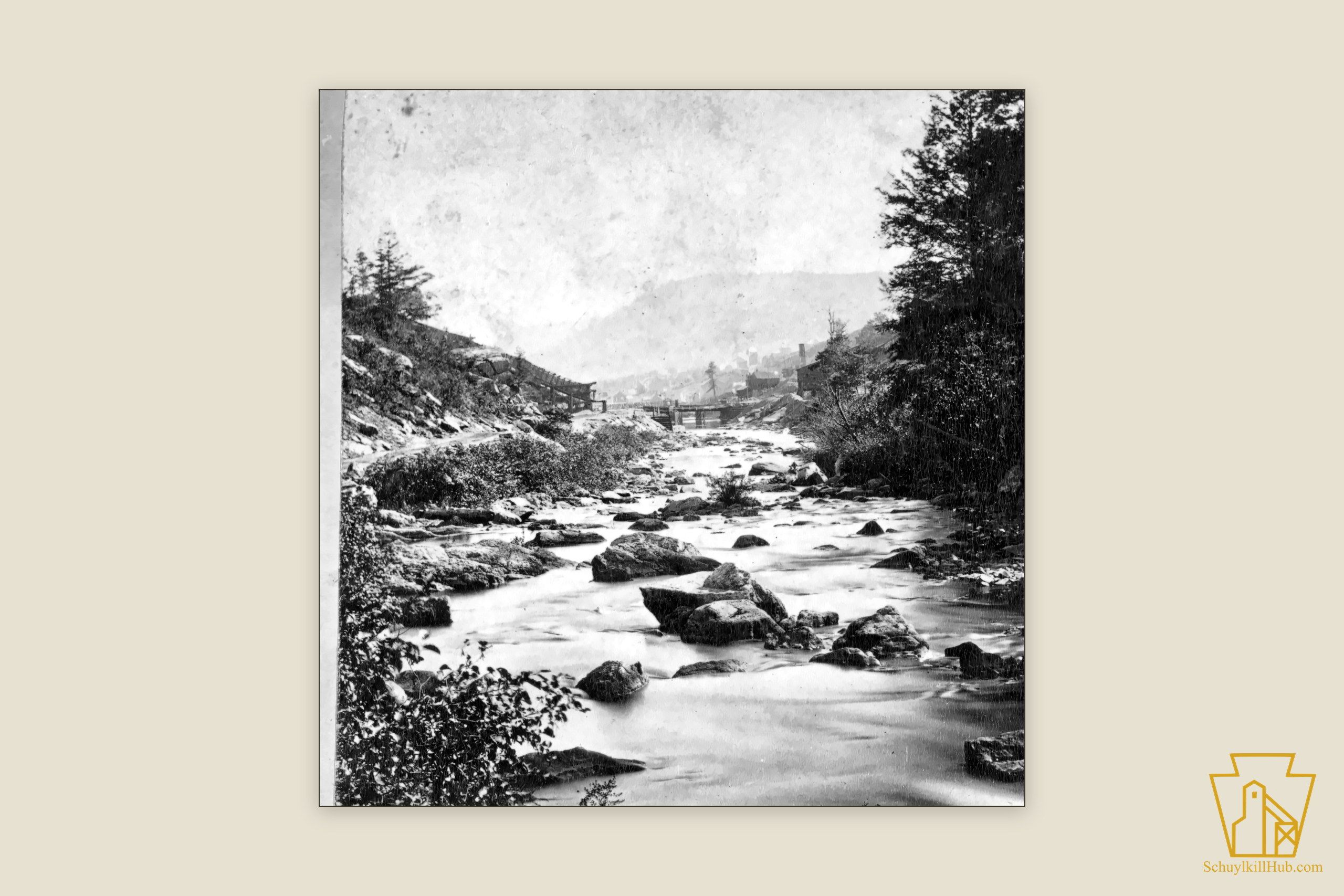 The Little Schuylkill tumbling over boulders below a forested gorge, a wooden footbridge and mill settlement beyond.