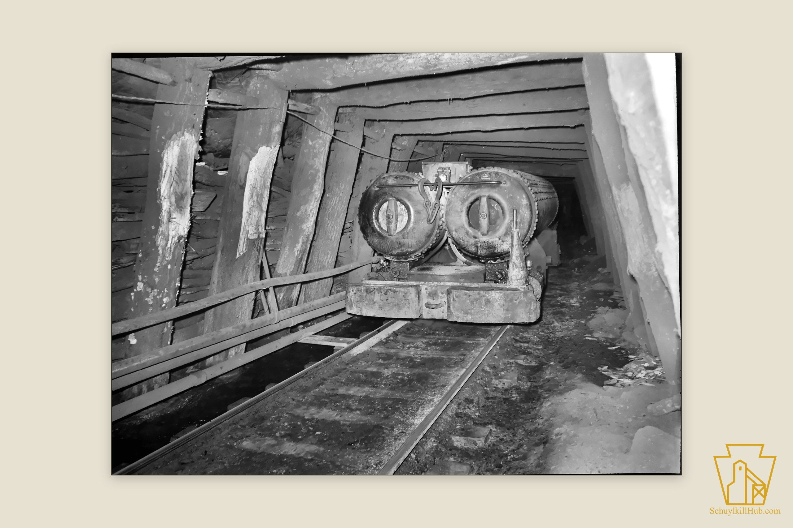 A compressed-air haulage engine and mine cars in a timbered underground gangway, air pipes beside the track.