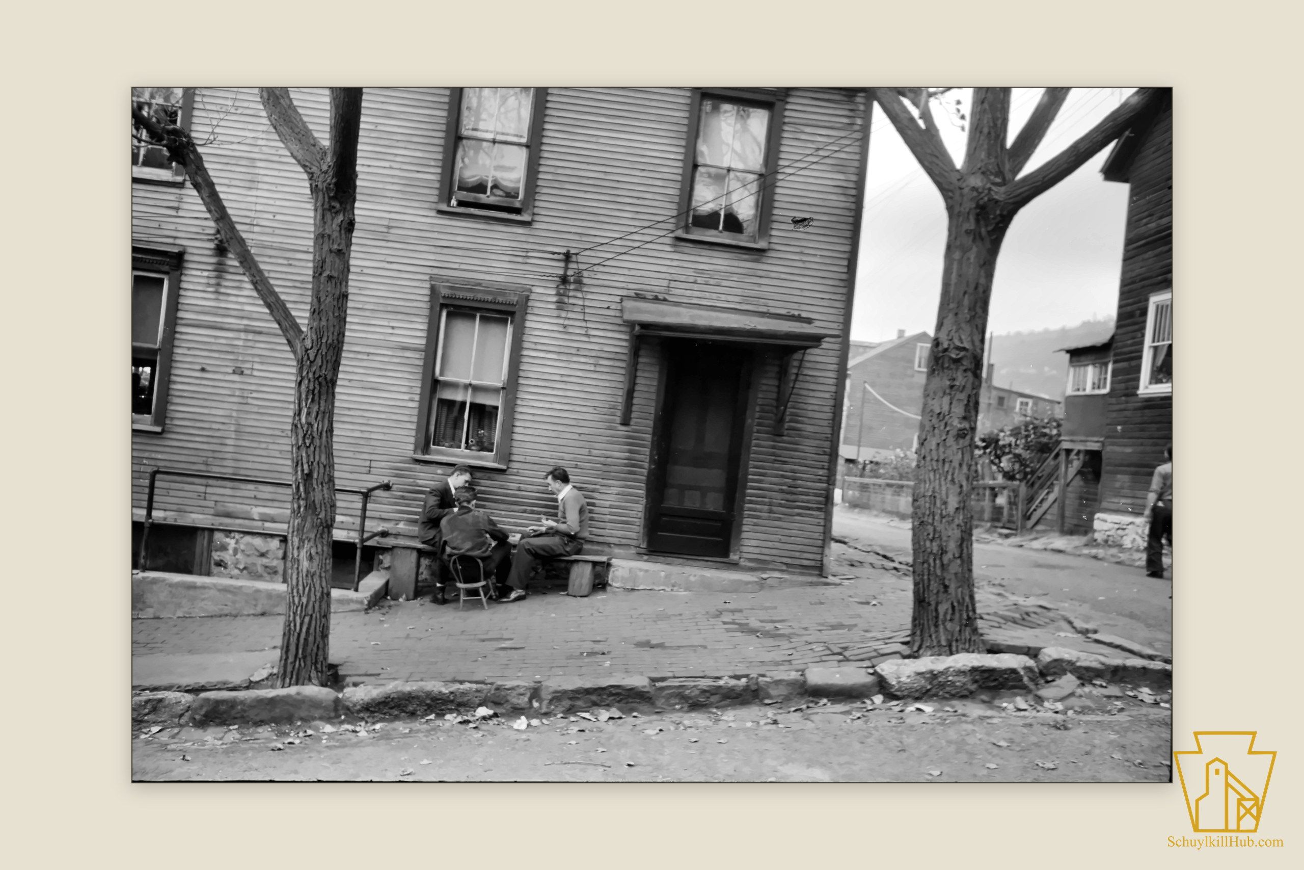 Three men playing a board game on a plank bench outside a weatherboard house.
