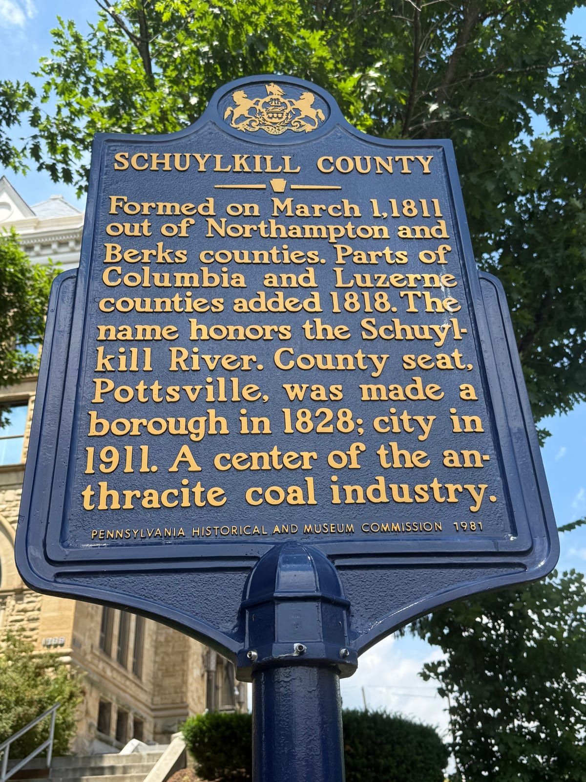 Pennsylvania's blue-and-gold state historical marker titled 'Schuylkill County,' on a post outside the Pottsville courthouse.